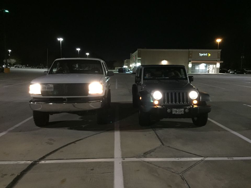 White Ford truck and silver Jeep Wrangler parked in a lot at night.