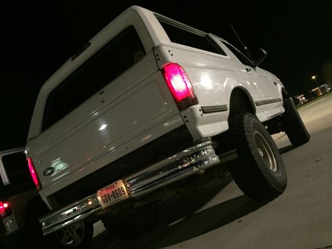 1996 Ford Bronco - The rear passenger side of a white 1996 Ford Bronco is shown at night. The vehicle has a Texas license plate reading "GDV-8609" and a chrom…