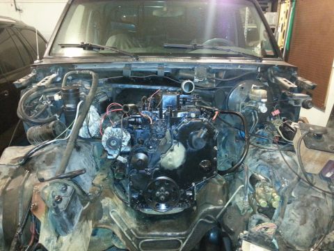 1994 Ford Bronco - The engine bay of a vehicle is shown with the engine partially disassembled. Various hoses, wires, and engine components are visible.