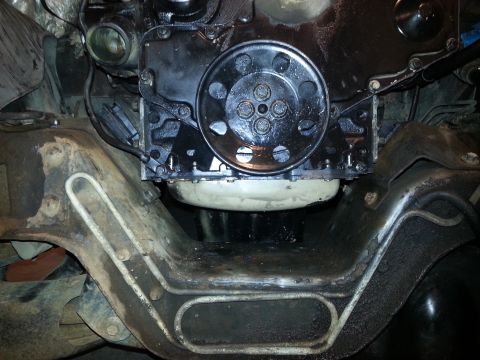 1994 Ford Bronco - This image shows the underside of a vehicle, focusing on the engine and frame components. A black engine block with a circular pulley is vi…