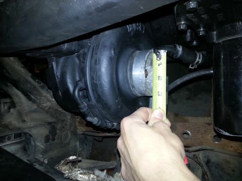 1994 Ford Bronco - A hand holds a yellow measuring tape against a black turbocharger assembly mounted in an engine bay. The tape is positioned to measure the…