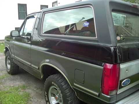 1992 Ford Bronco - The rear quarter panel of a black 1992 Ford Bronco is visible, with chrome trim and a Ford emblem on the tailgate.