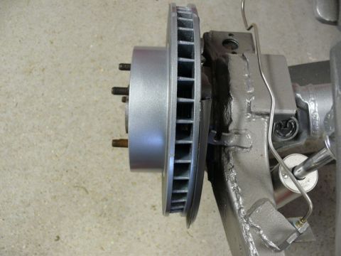 Silver brake rotor with studs attached to a gray suspension component with brake line.