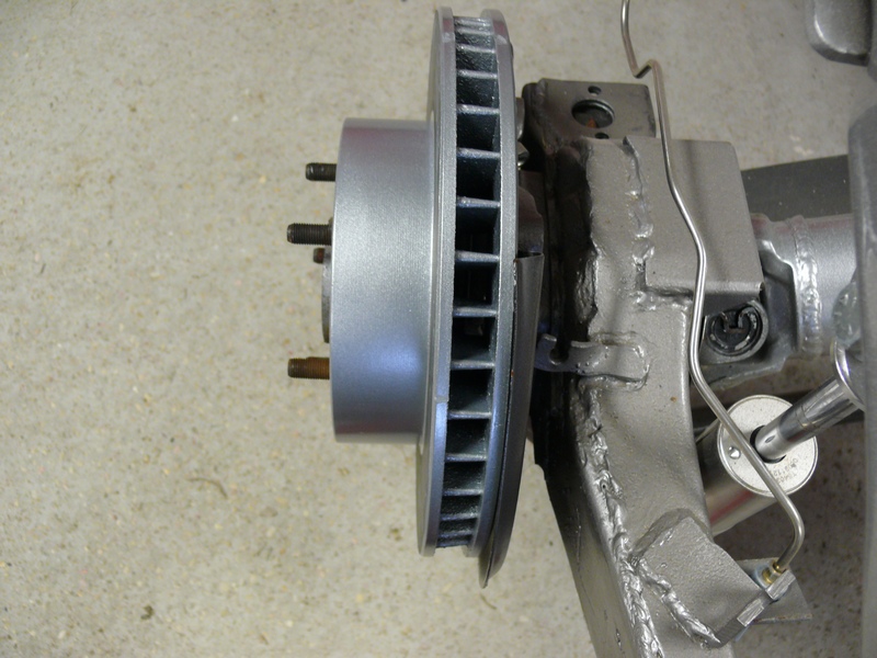Silver brake rotor with studs attached to a gray suspension component with brake line.