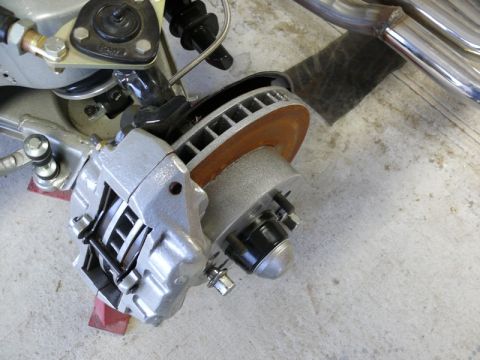 Close-up of a silver brake caliper, rusty rotor, and suspension parts on a vehicle.