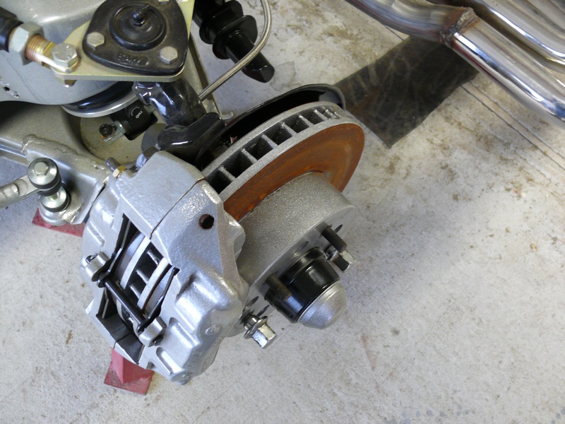 Close-up of a silver brake caliper, rusty rotor, and suspension parts on a vehicle.