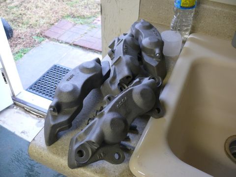 Four gray painted brake calipers on a countertop next to a sink.