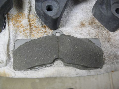 Close-up of a gray brake pad with a metal backing on a white cloth.