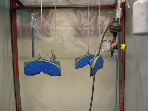 Two brake calipers with blue and green tape hanging in a spray booth.
