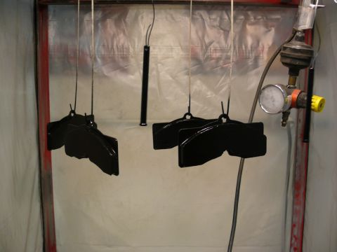 Black brake calipers hanging in a spray booth with a pressure regulator and gauge.