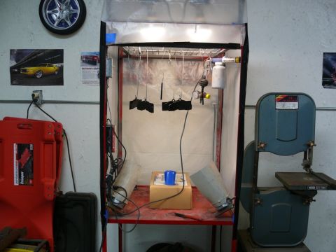 Spray booth with hanging parts, bandsaw, and red creeper.
