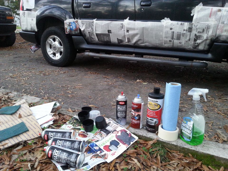 Dark pickup truck with newspaper-covered lower body panels and cleaning supplies on the ground.