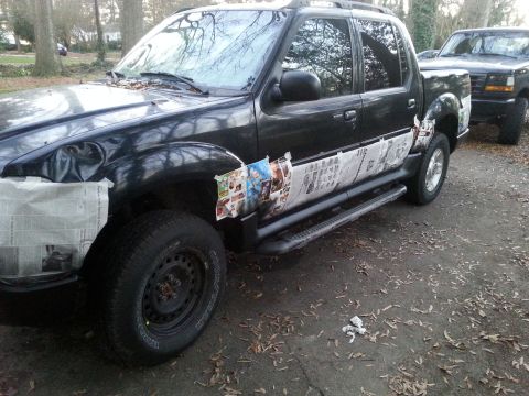 2001 Ford Explorer - A black Ford Explorer is parked outdoors with newspaper taped to the lower body panels and fender. Another black Ford pickup truck is parke…