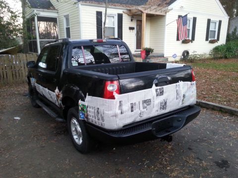 2001 Ford Explorer - A black Ford Explorer Sport Trac pickup truck is parked in a driveway with its bed and lower body panels covered in newspaper, possibly for…