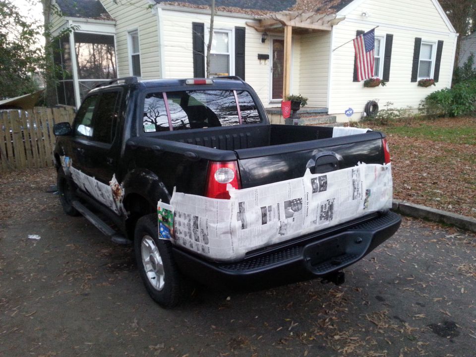 Black Ford Explorer Sport Trac pickup truck with newspaper covering the bed and lower body panels.