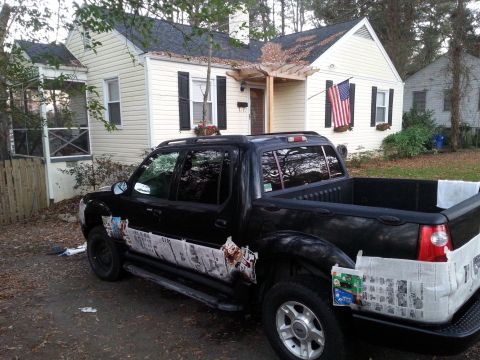 2001 Ford Explorer - A black Ford Sport Trac pickup truck is parked in a driveway in front of a light-colored house. The truck's body is decorated with newspape…