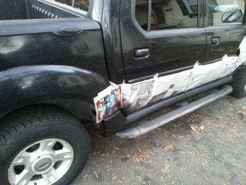 2001 Ford Explorer - The rear passenger side of a black Ford Sport Trac pickup truck is shown with newspaper taped to the lower body panel near the rear wheel w…