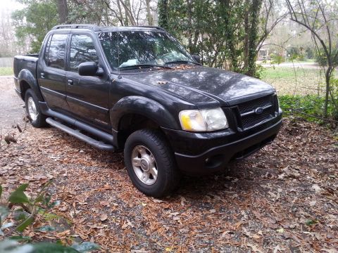 2001 Ford Explorer - A black 2001 Ford Explorer Sport Trac is parked on a gravel and leaf-covered surface surrounded by trees. The front passenger side of the t…
