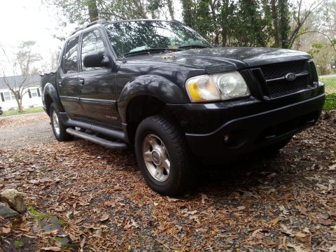 2001 Ford Explorer - A black Ford Explorer Sport Trac is parked on a gravel driveway covered in fallen leaves. The front passenger side of the truck is angled t…