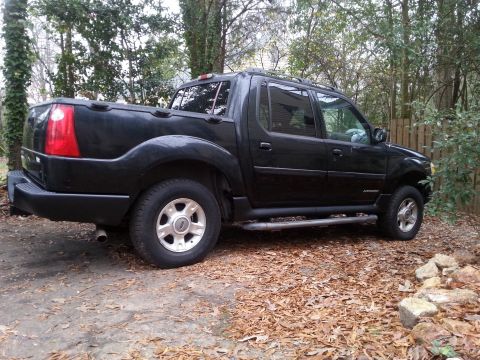 2001 Ford Explorer - The side profile of a black Ford Explorer Sport Trac is shown parked on a dirt and leaf-covered ground. The vehicle has a step bar, silver…