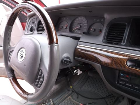 1999 Mercury Grand Marquis - The interior of a Mercury Grand Marquis is shown, focusing on the steering wheel and dashboard. The steering wheel has wood grain accents a…