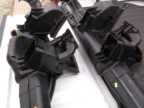 1999 Mercury Grand Marquis - Two black plastic HVAC duct assemblies are piled on top of each other on a white surface. Yellow stickers are visible on some of the parts.