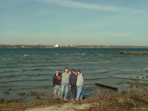 1978 Ford Bronco - A group of friends pose for a photo on a sandy shore with choppy water and a distant cityscape.