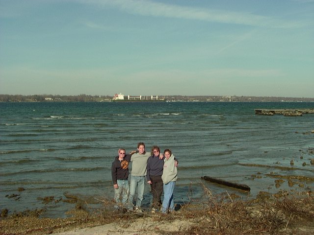 four people stand on a beach with water and a distant ship behind them