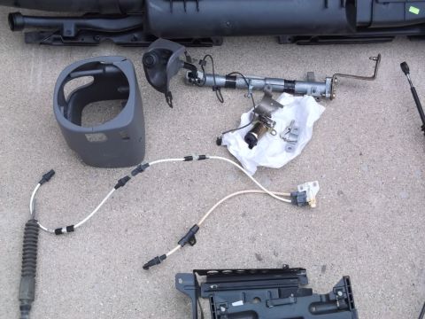 1999 Mercury Grand Marquis - Various car parts are laid out on a concrete surface. Visible items include a steering column shroud, cables, and a metal bracket with a so…
