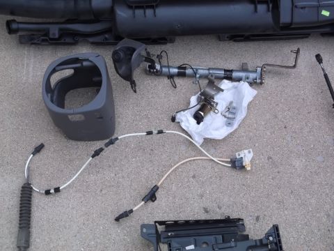 1999 Mercury Grand Marquis - Disassembled car parts, including a dark gray steering column shroud, a metal steering column assembly with cables, and other components, a…