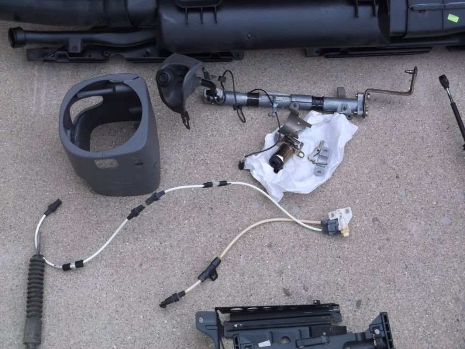 Disassembled car parts on concrete, including steering column shroud and assembly.