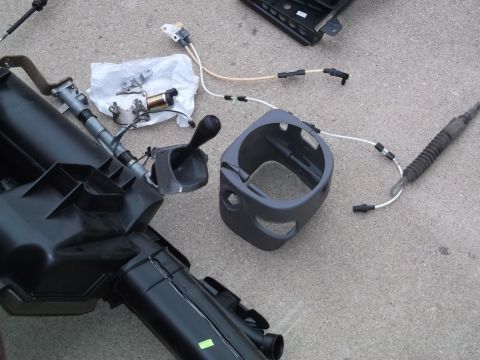 1999 Mercury Grand Marquis - Disassembled car parts, including a black plastic air duct system, a gear shifter, and a gray plastic steering column shroud, are laid out…