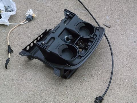 1999 Mercury Grand Marquis - A black car center console part with two cup holders, a coin holder, and a cable is shown on a concrete surface.