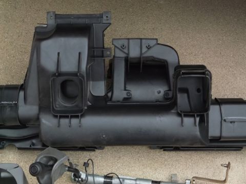 1999 Mercury Grand Marquis - This is a close-up, overhead shot of a black plastic air intake manifold system, likely from a vehicle. The part is laid out on a textured,…