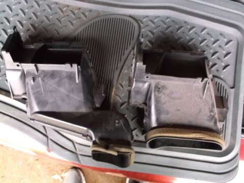 1999 Mercury Grand Marquis - Two black plastic HVAC ducting components are shown from a top-down perspective, resting on a textured gray mat. The components appear to b…