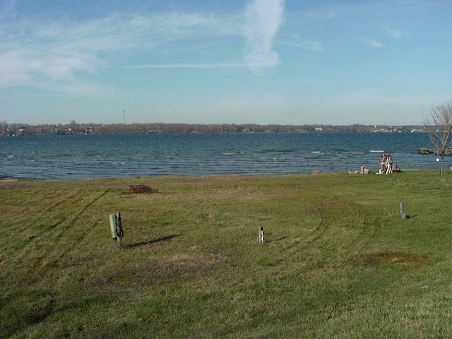 Grassy field with a body of water and a distant treeline under a cloudy sky