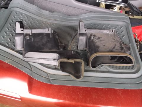 1999 Mercury Grand Marquis - Two black plastic HVAC ducting components with foam seals are laid out on a gray floor mat inside a vehicle. The components appear to be fo…