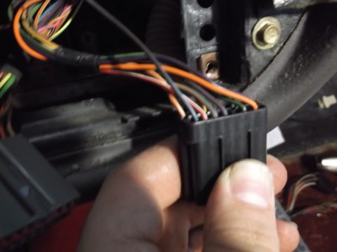 1999 Mercury Grand Marquis - A hand is holding a black electrical connector with multiple colored wires protruding from it. In the background, other wiring harnesses an…