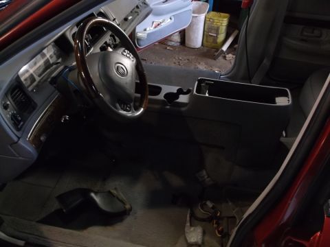 1999 Mercury Grand Marquis - The interior of a red Mercury Grand Marquis shows the driver's side dashboard, steering wheel, and center console. Wires and parts are visi…
