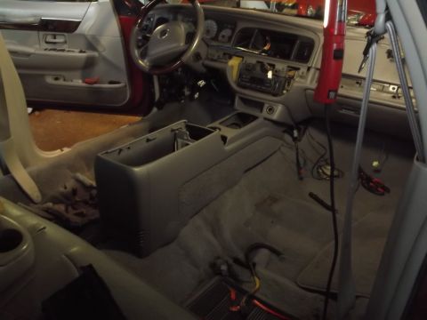 1999 Mercury Grand Marquis - The interior of a vehicle is shown with the dashboard and center console disassembled. Tools and wiring are visible on the floor and consol…
