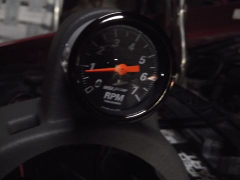 1999 Mercury Grand Marquis - A close-up view of a black tachometer gauge with an orange needle, mounted on a dark gray dashboard. The gauge displays RPMs and is partial…