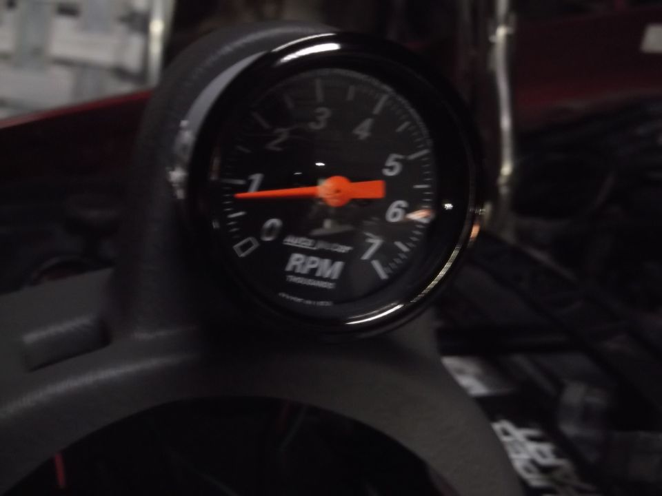Close-up of a black tachometer gauge with an orange needle on a car dashboard.