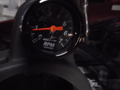 1999 Mercury Grand Marquis - A close-up shot of an AutoMeter RPM gauge with a red needle pointing slightly past the 1,000 RPM mark. The gauge is mounted on a dark dashb…