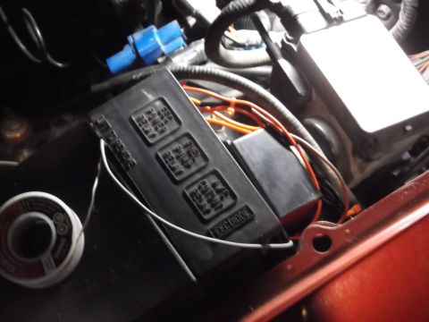 1999 Mercury Grand Marquis - A close-up view of a black automotive fuse box with multiple relays and wiring, along with a roll of solder, is visible in an engine bay.