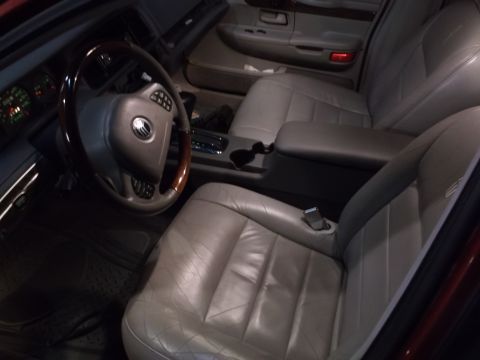 1999 Mercury Grand Marquis - The interior of a car is shown, featuring a leather steering wheel with wood trim and a gray leather driver's seat. The dashboard and cente…