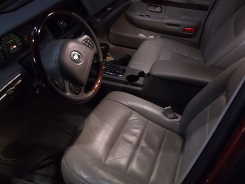 1999 Mercury Grand Marquis - The interior of a car shows a leather steering wheel with wood trim and a grey leather driver's seat. The center console with cup holders a…