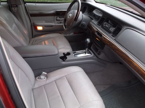 1999 Mercury Grand Marquis - The interior of a 1999 Mercury Grand Marquis shows light gray leather seats, a wood-grain trim dashboard, and a center console with a gear…
