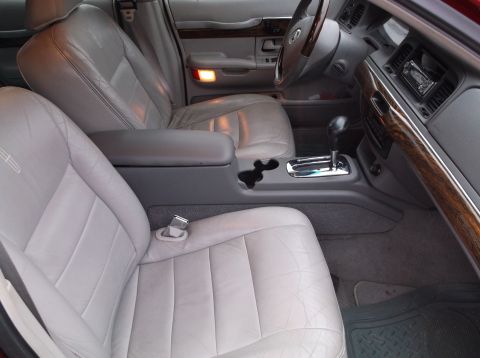 1999 Mercury Grand Marquis - The interior of a 1999 Mercury Grand Marquis shows the front passenger seat and center console. The light gray leather seats and wood grain…