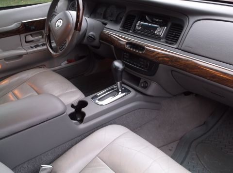 1999 Mercury Grand Marquis - The interior of a car shows the driver's side door panel, steering wheel, dashboard with a radio, and the center console with a gear shifte…