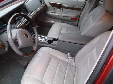 1999 Mercury Grand Marquis - The interior of a red 1999 Mercury Grand Marquis is shown, featuring light gray leather seats, a wood-trimmed steering wheel, and a center…